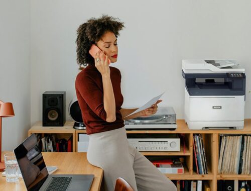 A woman sitting at a desk having a call next to a Xerox® C325 Printer