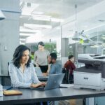 Professional woman typing on laptop at desk in office environment next to a Xerox® C325 Printer