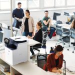 A group of professionals collaborating in an office, utilising computers and Xerox® VersaLink® B625 for their tasks.