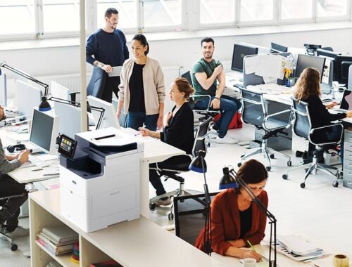 A group of professionals collaborating in an office, utilising computers and Xerox® VersaLink® B625 for their tasks.